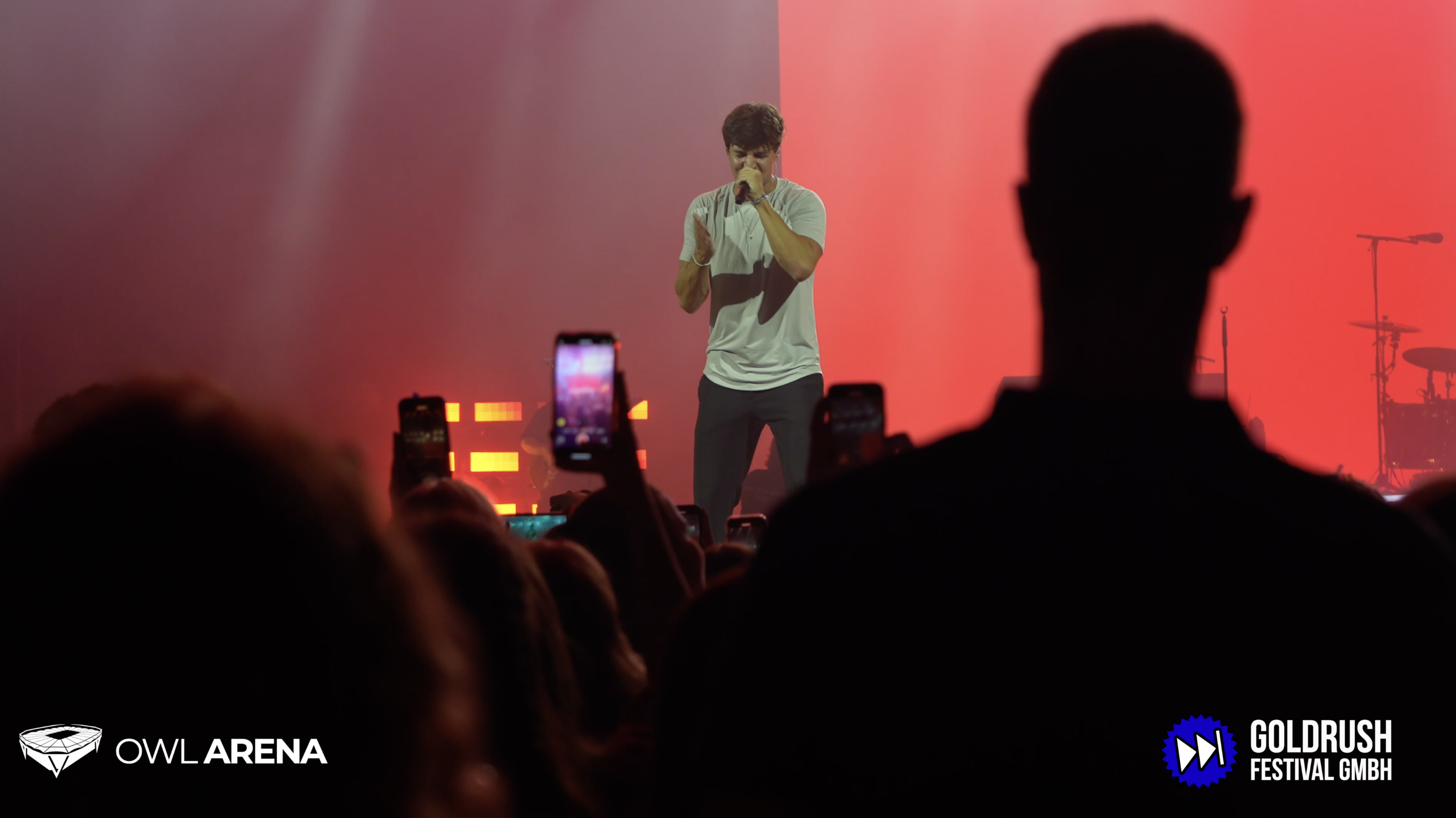 Ein Sänger performt auf einer Bühne, umgeben von begeisterten Fans, die ihre Smartphones hochhalten.