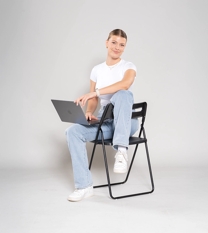 Eine Person sitzt entspannt auf einem schwarzen Klappstuhl und arbeitet konzentriert an einem Laptop.