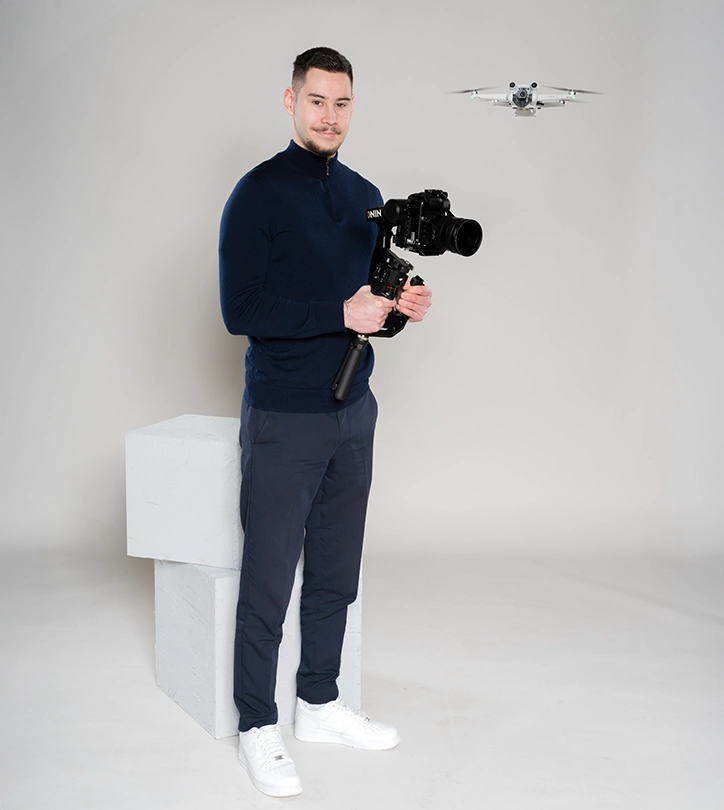 Mann mit Kamera und Gimbal, Drohne im Hintergrund, professionelle Aufnahmeumgebung.