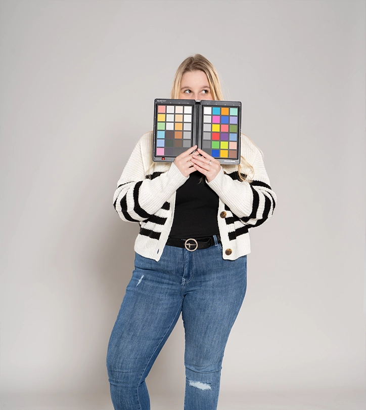 Person hält Farbkalibrierungs-Chart vor Gesicht, trägt gestreifte Strickjacke und blaue Jeans.