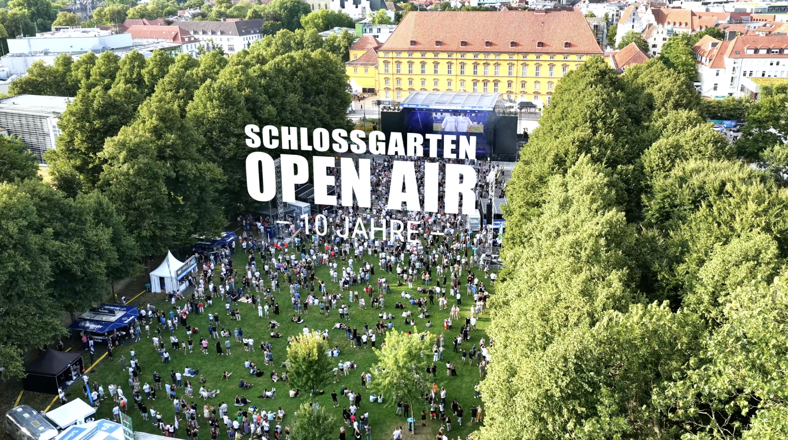 Luftaufnahme eines Open-Air-Konzerts im Schlossgarten mit großer Menschenmenge und historischer Kulisse.